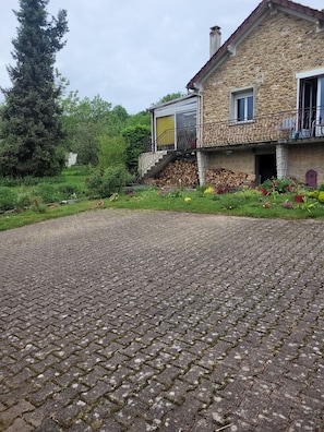 A stone house with a paved driveway, a wooden staircase, and a garden with various plants. - Vrbo Property (Pommeuse)