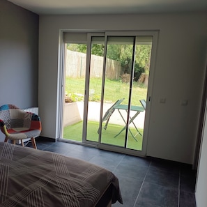 A room with a bed, a chair, and a sliding glass door leading to an outdoor area with a table and chairs. - Vrbo Property (Pommeuse)