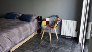 A bedroom with a bed, a chair, a radiator, and a picture on the wall.