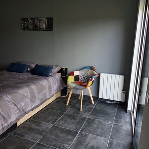 Un dormitori amb un llit, una cadira, un radiador i un quadre a la paret.
