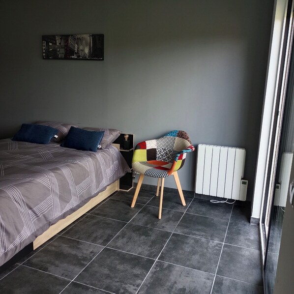 A bedroom with a bed, a chair, a radiator, and a picture on the wall.