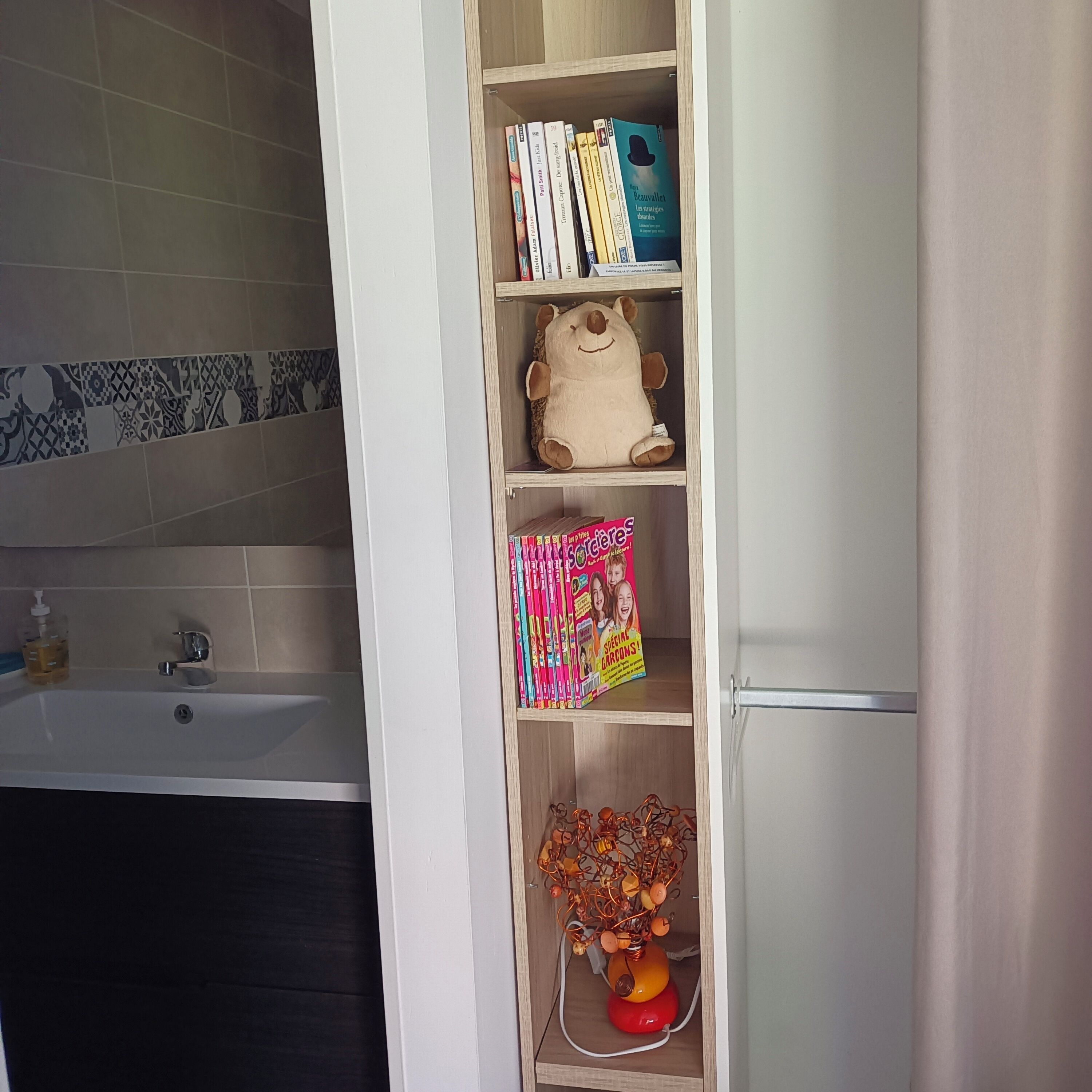 Ett badrum med ett badkar, en hylla med böcker och en mjuk leksak samt en dekorativ detalj på den nedre hyllan.