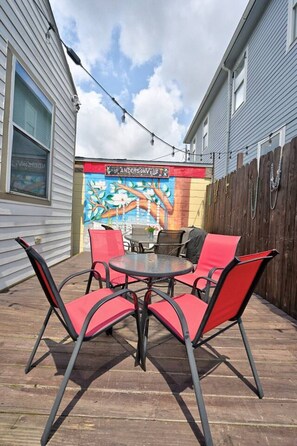 An outdoor patio with a table and chairs, a mural on the wall, and a wooden fence. - 2BR Home 1 Block to Streetcar, Near French Quarter (New Orleans)