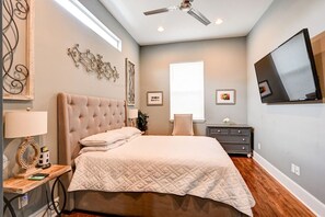 A bedroom with a large bed, a ceiling fan, a TV mounted on the wall, and a window with blinds. - 2BR Home 1 Block to Streetcar, Near French Quarter (New Orleans)