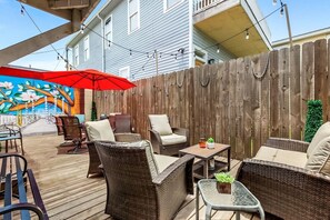 An outdoor patio area with wicker furniture, a red umbrella, and a wooden fence. - 2BR Home 1 Block to Streetcar, Near French Quarter (New Orleans)