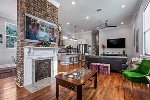 A modern living room with a fireplace, a dining area, a kitchen, and a television mounted on the wall. - 2BR Home 1 Block to Streetcar, Near French Quarter (New Orleans)