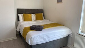 Ein Bett mit grauem Kopfteil, weißer Bettwäsche und einer senfgelben Decke.