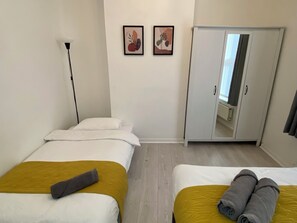 Ein Hotelzimmer mit zwei Betten, einem Kleiderschrank und zwei gerahmten Kunstwerken an der Wand.
