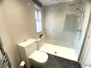 Une salle de bain moderne avec une douche à parois de verre, des toilettes blanches et un meuble-lavabo avec un miroir.