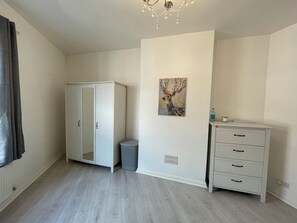 A room with a wardrobe, a trash bin, a radiator, and a wall-mounted artwork. - Free Parking | Near Co-op Live & Etihad | Entire 3-Bedrooms House Sleeps 7 (Manchester)