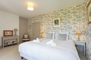 A neatly made bed with pillows and a rolled towel, a chair, a bedside table with a lamp, and a framed picture on the wall. - Manor House Near the Castles of the Loire Valley (Neuillé-Pont-Pierre)