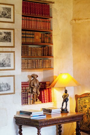 Um quarto com uma estante cheia de livros, uma estátua, uma mesa com livros e quadros nas paredes.