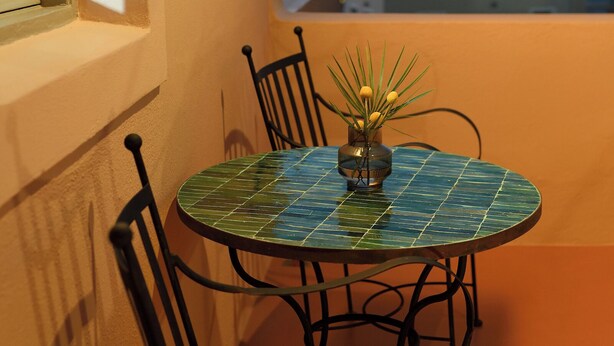Una mesa redonda con una cubierta de baldosas verdes, dos sillas negras y una pequeña planta en maceta.