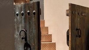A wooden gate leading to a staircase with a beige wall and a potted plant in the background. - Terra Verde Oia Suites - Terracote Grand Suite Sea View with Outdoor Jetted Tub (Oia)