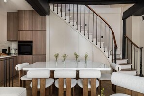 A modern kitchen with a dining area, featuring a glass-top table and white upholstered chairs. - Parisian Elegance: Stunning 3BR Retreat in the Heart of Le Marais (Paris)