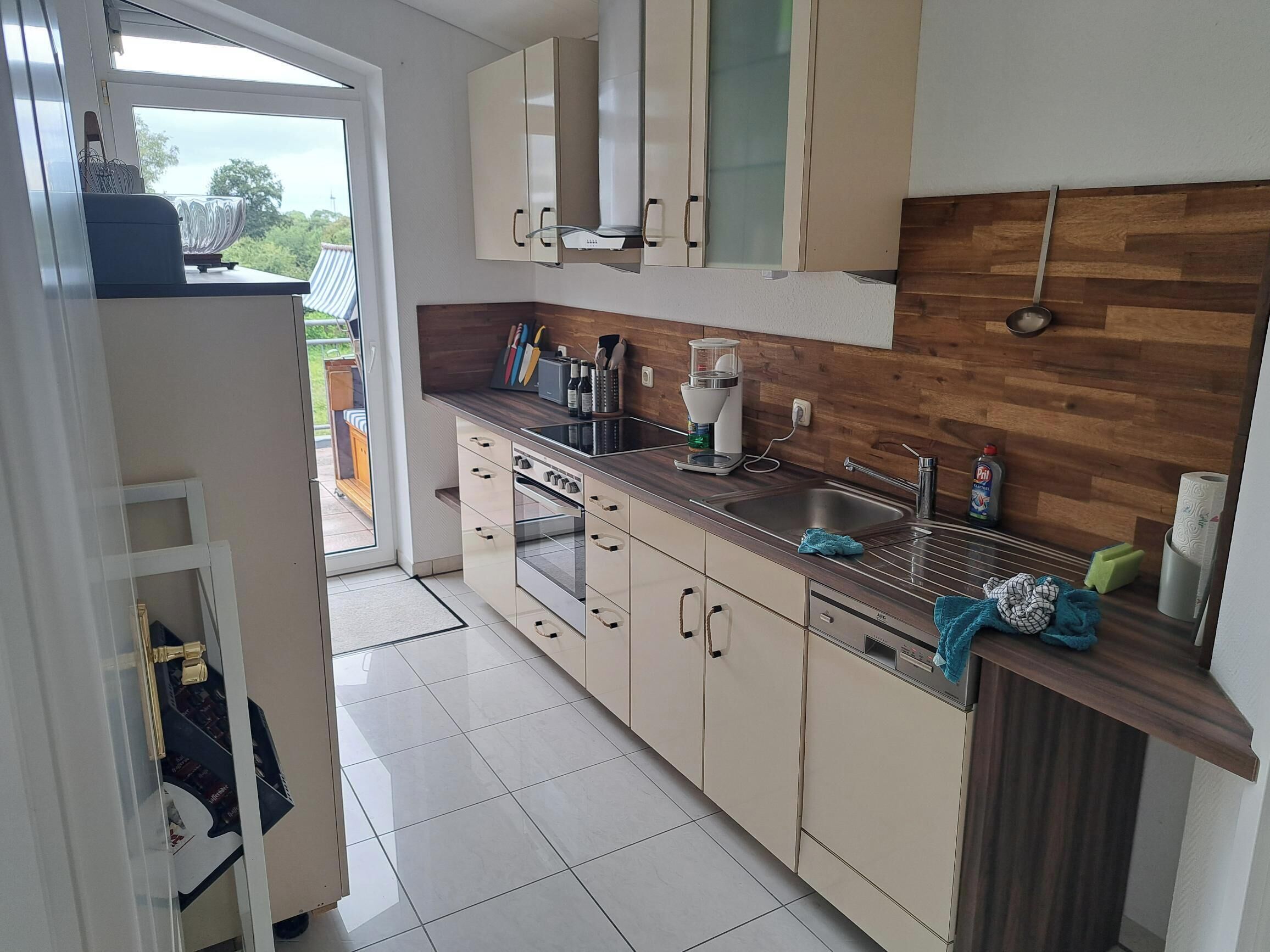 A modern kitchen with a wooden backsplash, stainless steel appliances, and a view through an open door to an outdoor area.