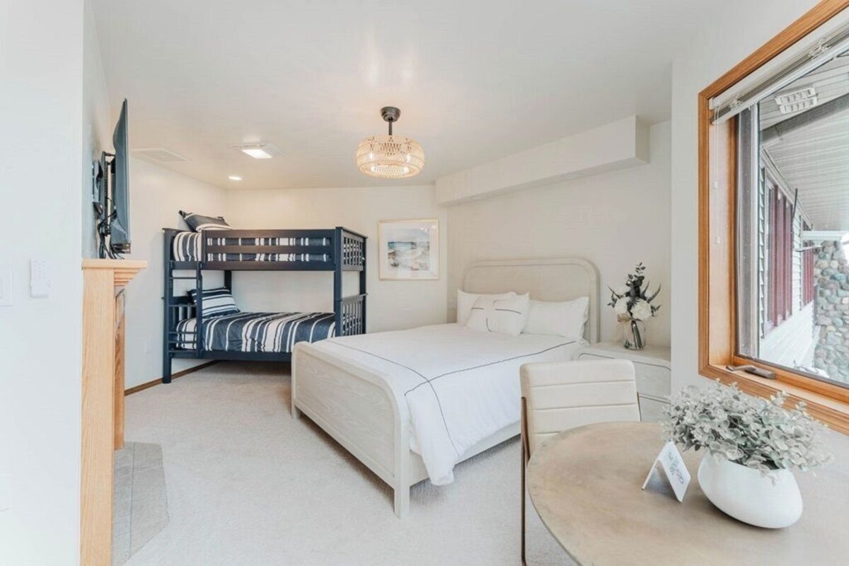 A bedroom with bunk beds, a single bed, a desk, a chair, a window with a view, and a chandelier.