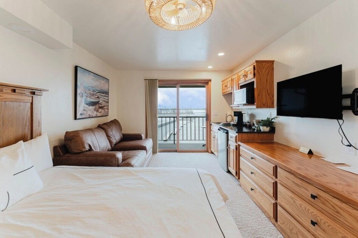 A bedroom with a large bed, a wooden dresser, a television, and a painting on the wall.