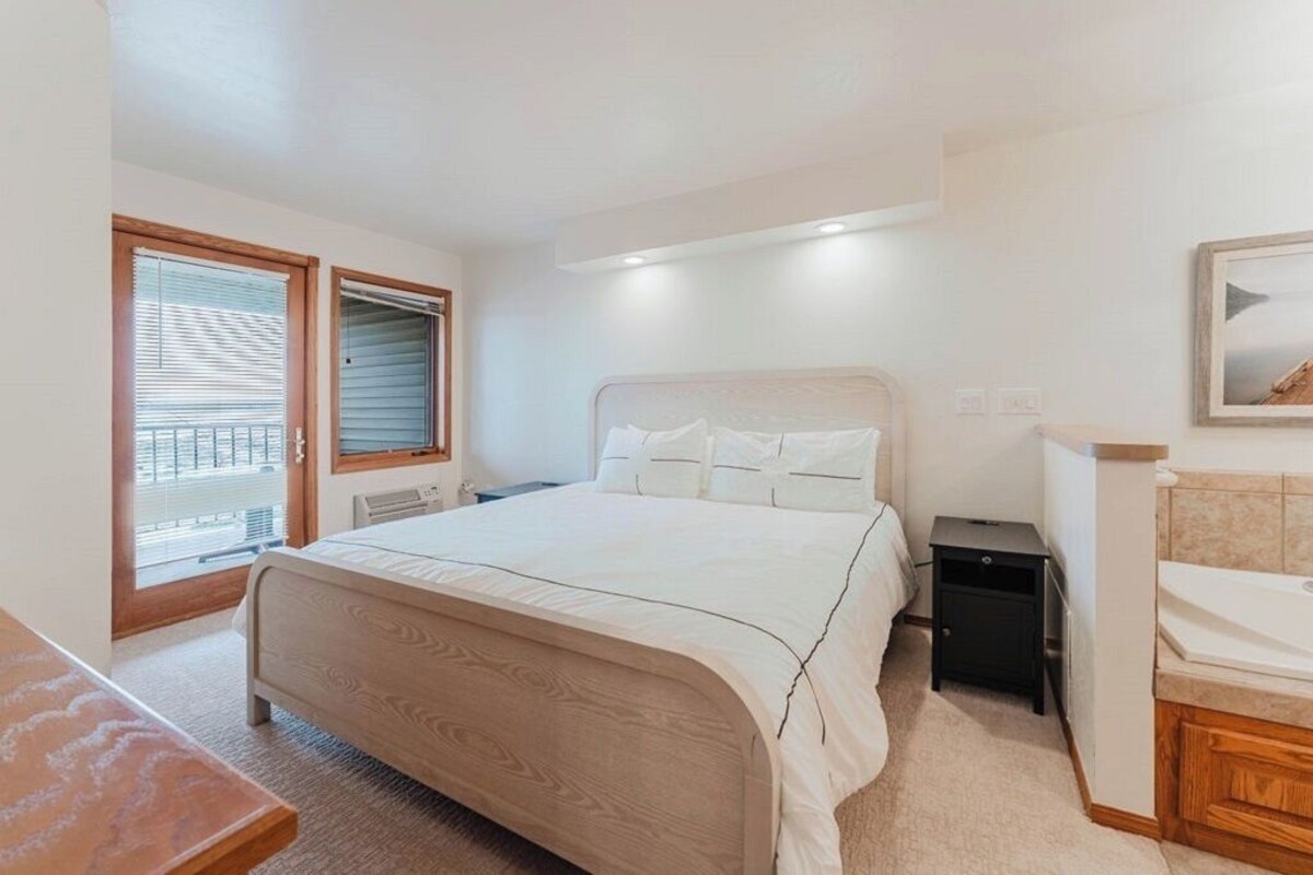 A bedroom with a bed, bedside table, and a window with blinds.