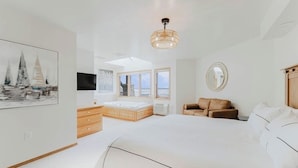 Quarto com cama grande, penteadeira de madeira, área de estar e televisão.