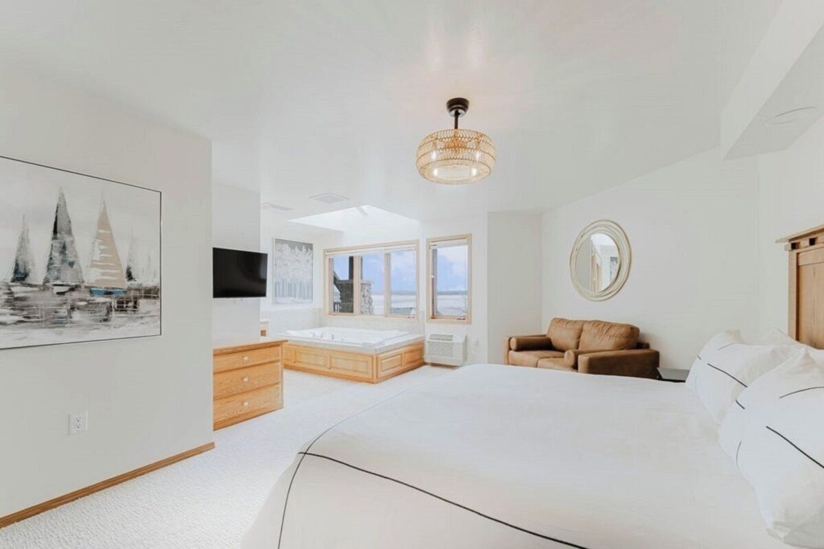 A bedroom with a large bed, a wooden dresser, a seating area, and a television.