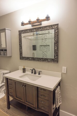 Une salle de bain avec un lavabo blanc, un meuble-lavabo en bois foncé et un miroir doté d’un cadre décoratif.