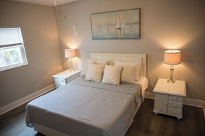 Une chambre à coucher avec un grand lit, deux tables de chevet, une commode, un tableau au mur et une fenêtre.