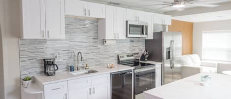 A modern kitchen with white cabinets, a stainless steel refrigerator, a microwave, and a dishwasher.