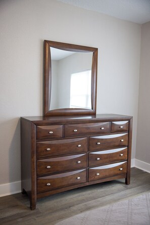 A wooden dresser with a mirror, drawers, and knobs, positioned against a wall with a window. - The Perfect Getaway (Clearwater)