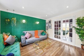 Een woonkamer met een groene wand, een grijze bank, een glazen salontafel en een potplant.