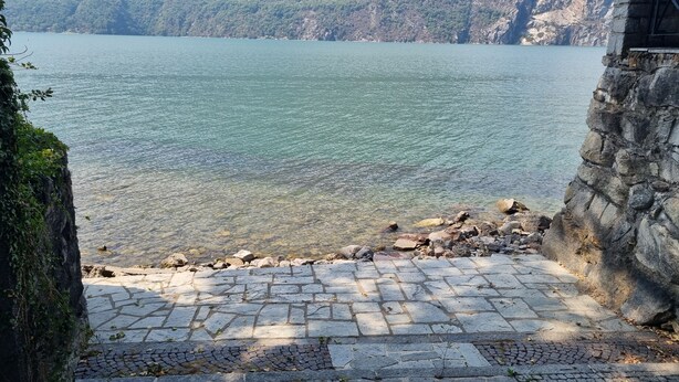 A stone pathway leading to a lake with clear water, surrounded by mountains.
