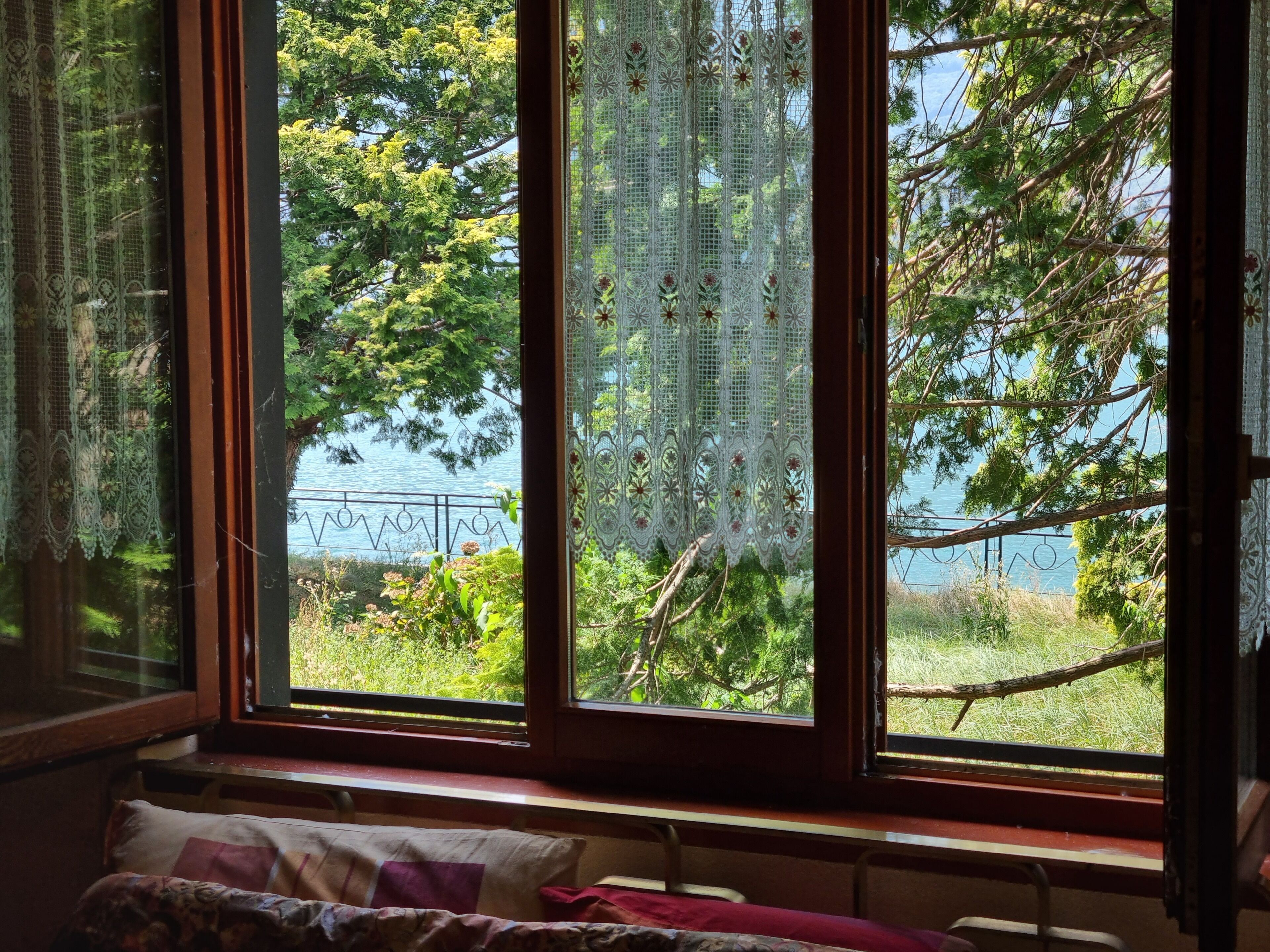 A room with a large window overlooking a natural landscape, a bed with a patterned bedspread, and a view of trees and a body of water.
