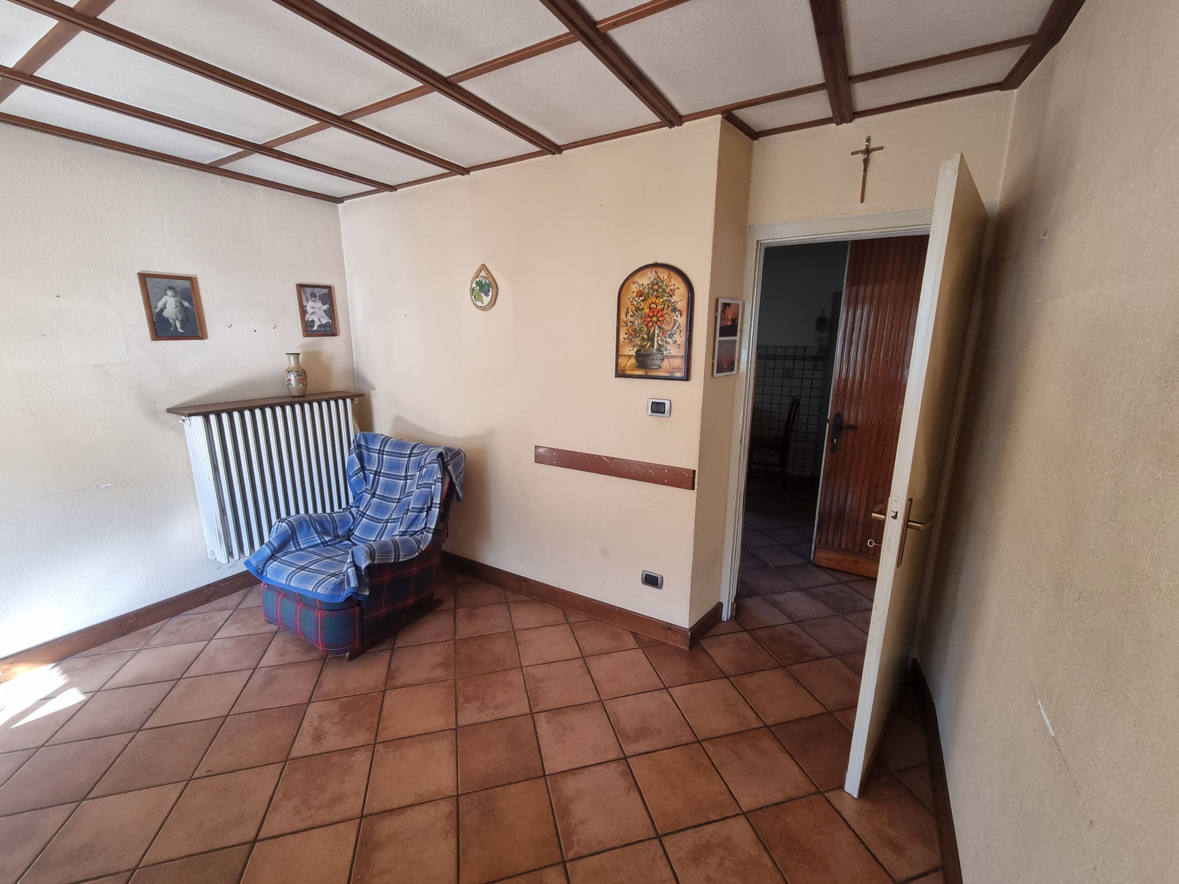 A room with a tiled floor, a blue plaid sofa, a radiator, and a door leading to another room.