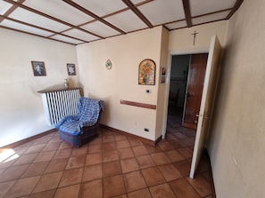 A room with a tiled floor, a blue plaid sofa, a radiator, and a door leading to another room.