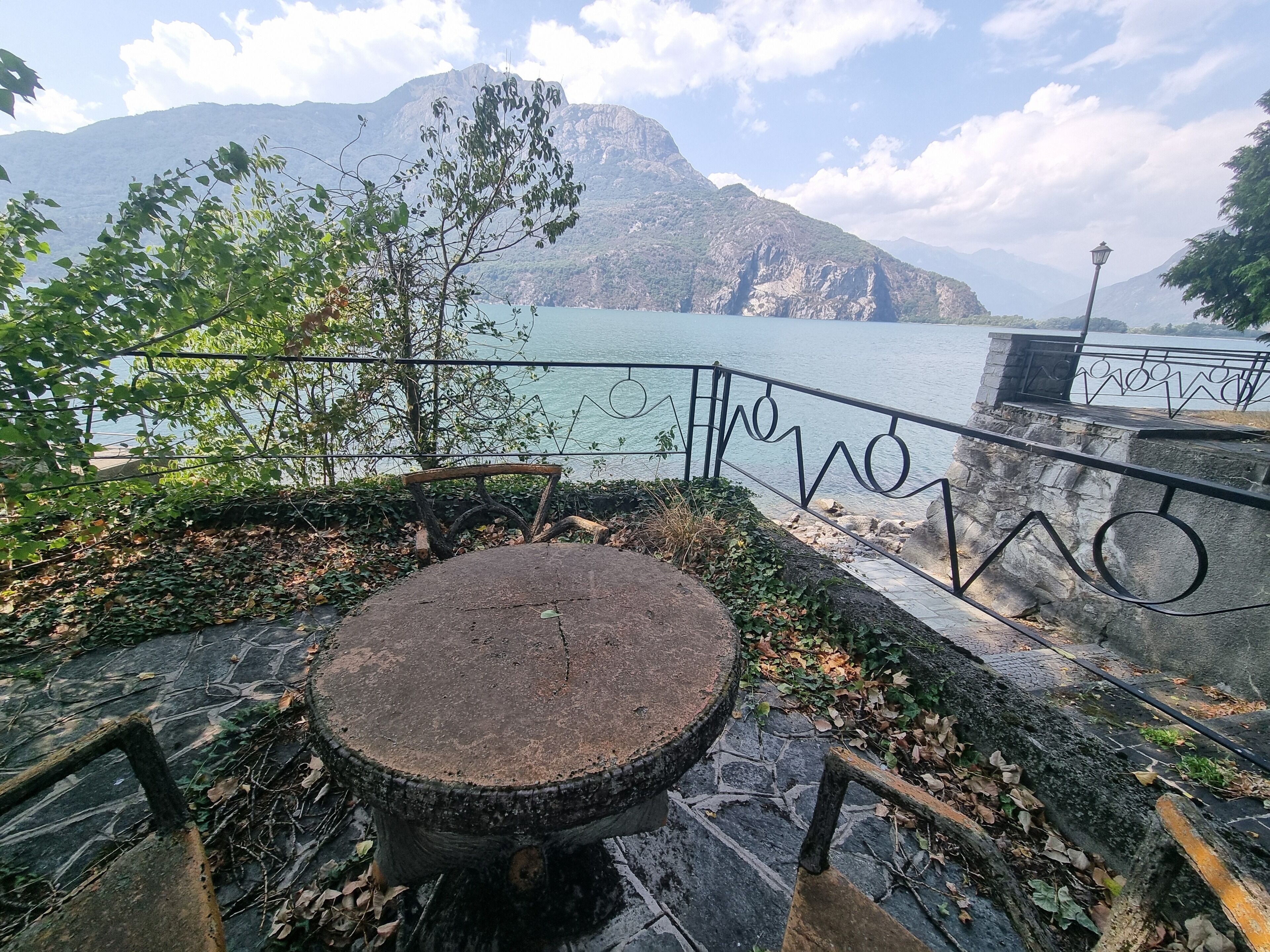 A stone bench with a metal railing overlooking a body of water and mountains.