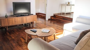 A living room with a flat-screen TV on a wooden cabinet, two round tables with remote controls, a sofa, and a staircase leading to another room. - Family-friendly apartment in Ravenna's historic center near UNESCO monuments (Ravenna)