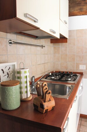 Eine Küche mit einem Gasherd, einer Edelstahl-Spüle, Holzkocherwerkzeugen und einem grünen Keramikbehälter.