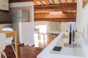 Eine moderne Küche mit integriertem Kühlschrank, Holzbalkendecke, Essbereich mit Tisch und Stühlen sowie Wohnbereich mit Sofa und rundem Tisch.
