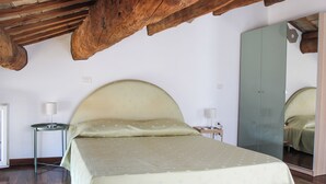 A bedroom with a large bed, wooden ceiling beams, a mirror, and a small bedside table with a lamp. - Family-friendly apartment in Ravenna's historic center near UNESCO monuments (Ravenna)