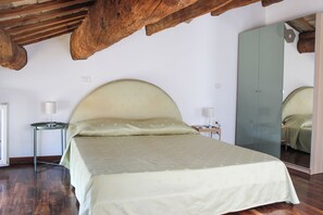 Een slaapkamer met een groot bed, houten balken in het plafond, een spiegel en een klein nachtkastje met een lamp.