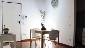A dining area with a wooden table, four chairs, a fruit bowl, and a wall-mounted light fixture. - Family-friendly apartment in Ravenna's historic center near UNESCO monuments (Ravenna)