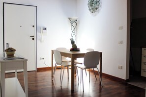 Een eetgedeelte met een houten tafel, vier stoelen, een fruitschaal en een wandlamp.