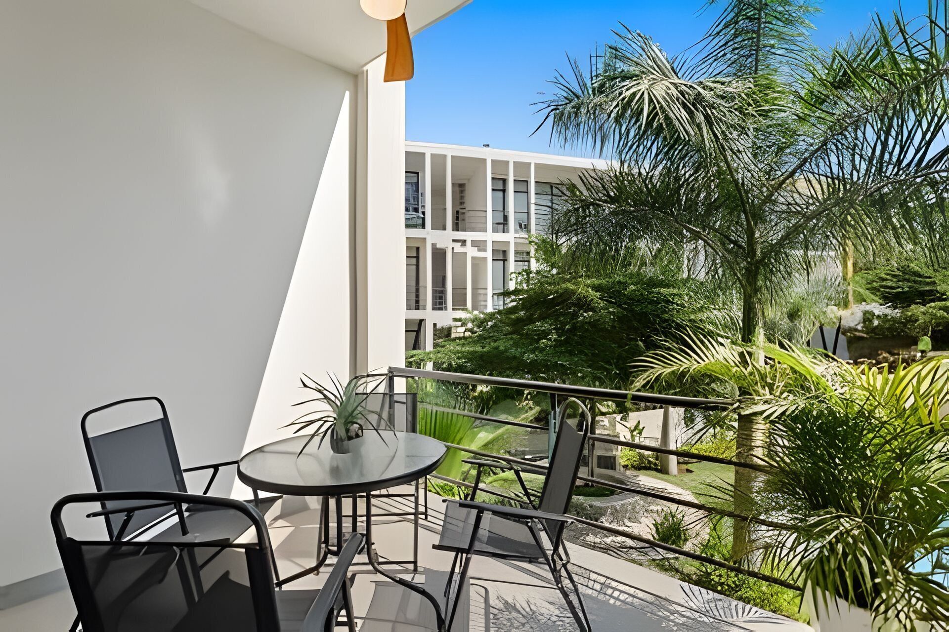 Un balcon avec deux chaises et une table, d’où l’on peut admirer un immeuble et une végétation luxuriante.