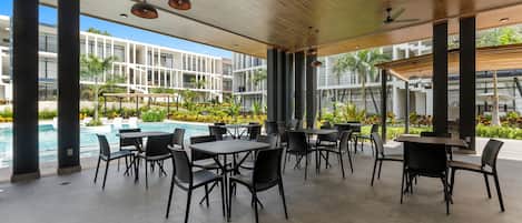 Un espacio al aire libre con mesas y sillas, piscina y vista a edificios modernos.