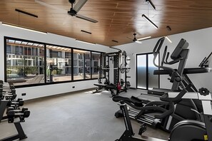 A gym with exercise equipment, large windows, and a view of a building outside. - Ground Floor · 2 Pools · Balcony · 15 min to Beach (Mezcales)