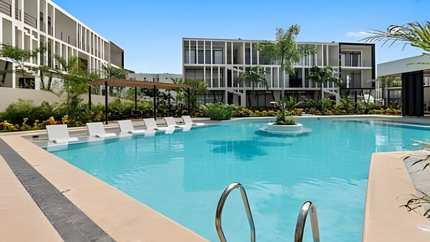 A modern pool area with clear blue water, surrounded by lounge chairs and a building with large windows. - Vrbo Property (Mezcales)
