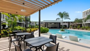 An outdoor pool area with tables and chairs, surrounded by greenery and modern buildings. - Vrbo Property (Mezcales)