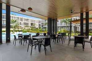 An outdoor seating area with tables and chairs, a pool, and a view of modern buildings. - Ground Floor · 2 Pools · Balcony · 15 min to Beach (Mezcales)