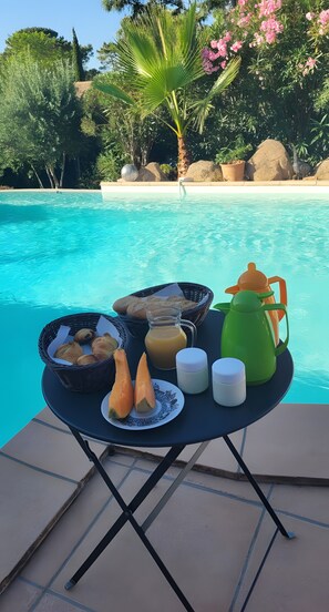 A poolside table with breakfast items, a bird, and a clear blue pool. - Bed and Breakfast "L'isula" with Mountain View, Wi-Fi, and Air Conditioning (Porto-Vecchio)