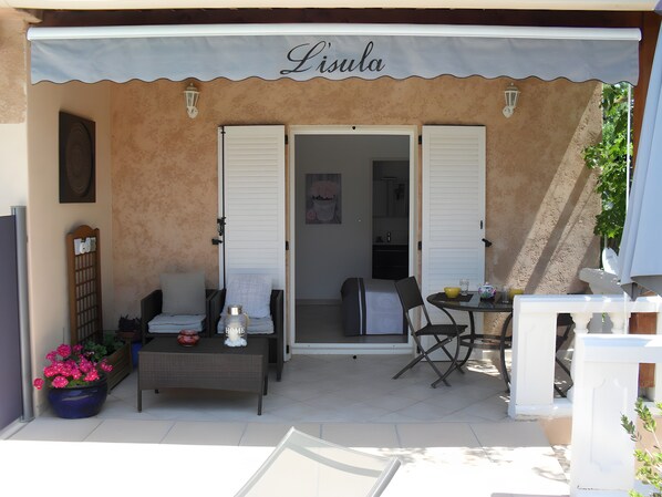 A covered outdoor seating area with a table and chairs, a potted plant, and a sign reading 'Lisula'.